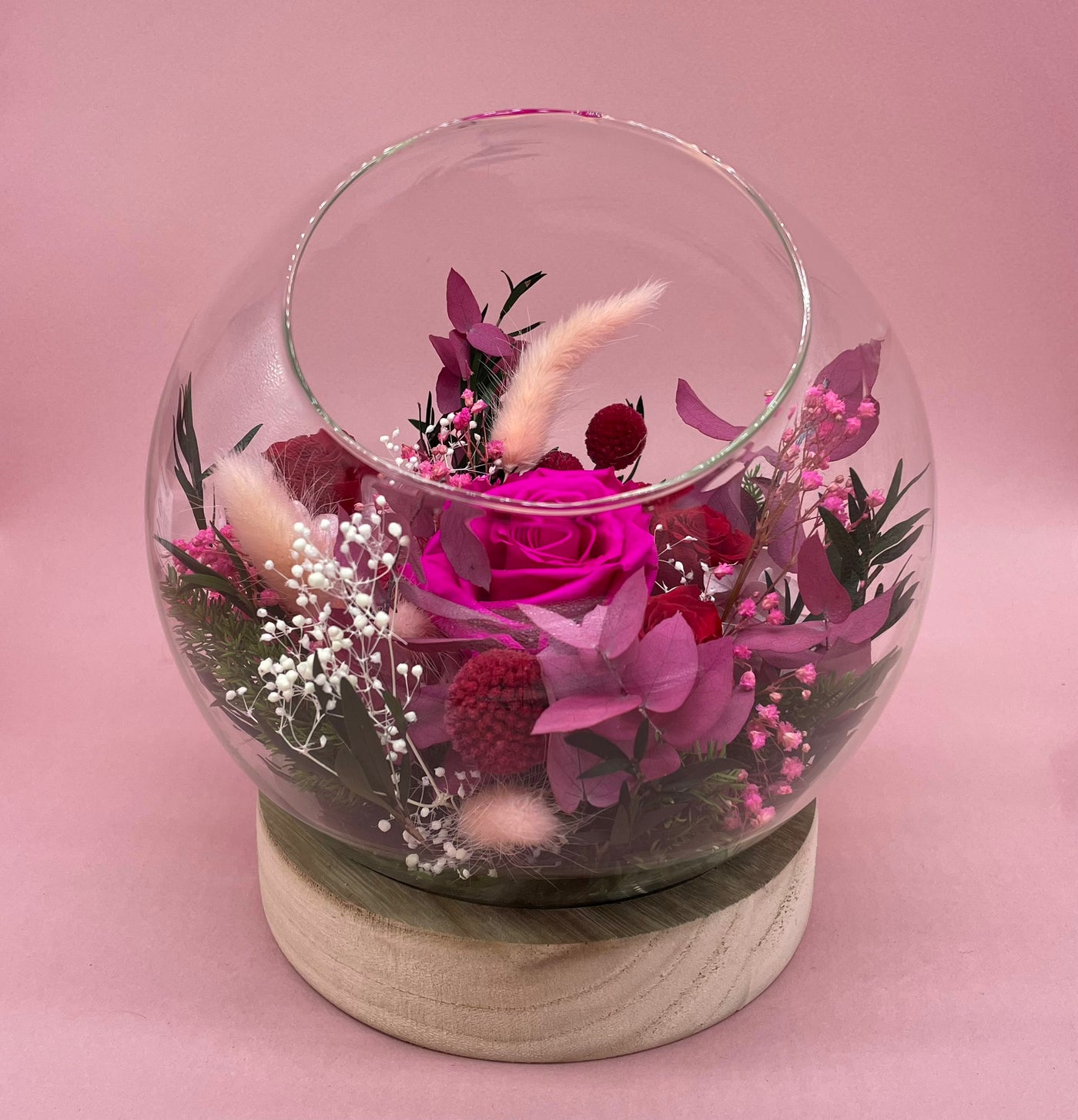 Bulle de verre avec socle en bois garni de fleur stabilisées sur des tonalités de rose et rouge Rose, Hortensia, Lagurus, Mini Gypsophile, Gypsophile, Craspedia & Eucalyptus stuartiana (vue de face)