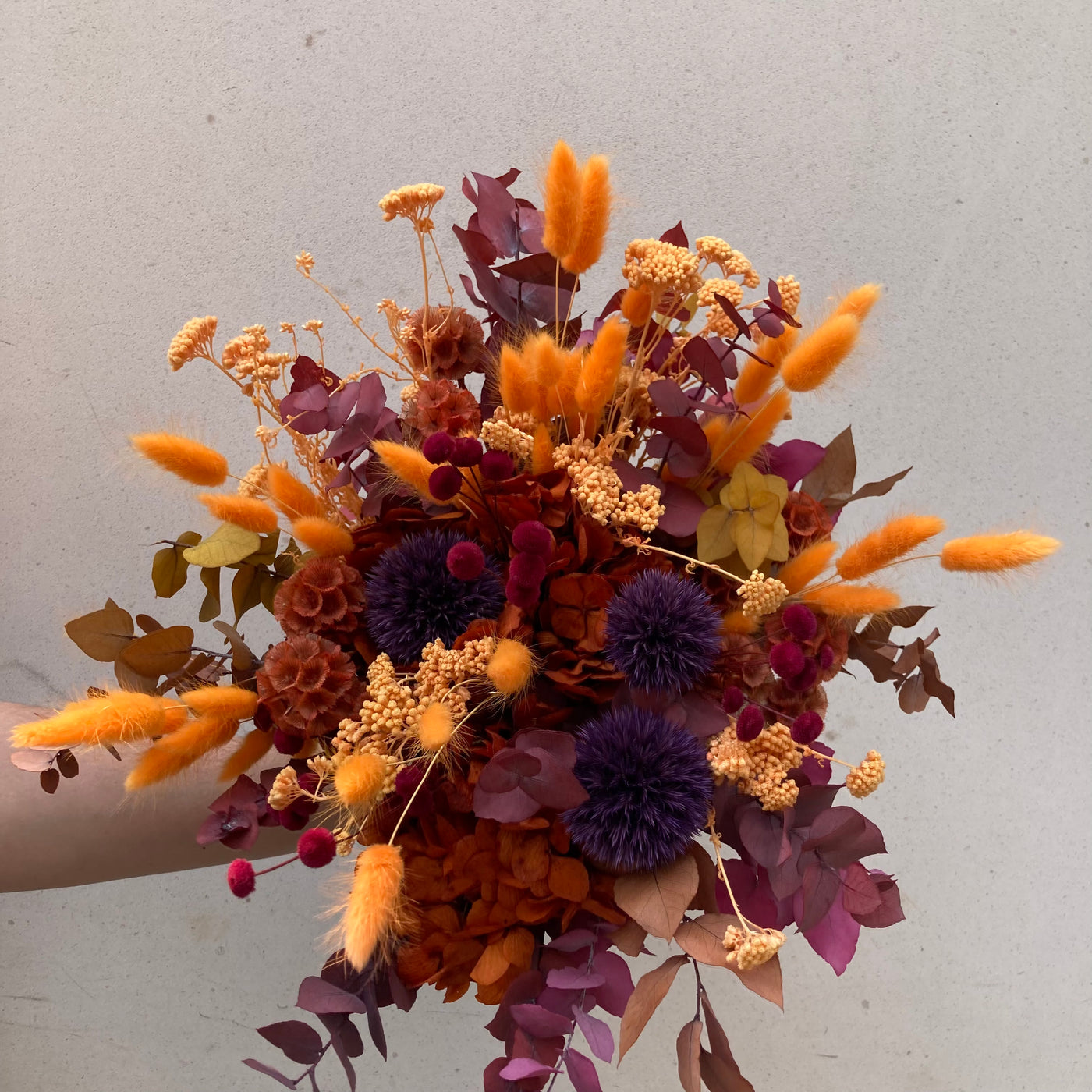 Bouquet en fleurs stabilisées éternelles orange et rouge composé de Lagurus, Chardon, Achillée, Botao, Scabieuse, Eucalyptus, Hortensia. Vu de face