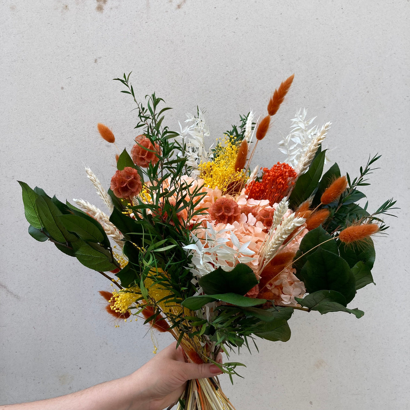 Bouquet en fleurs stabilisées éternelles orange et vert composé de Hortensia, scabieuse, blé, Lepto, Ruscus, Broom, Lagurus, Salal. Vu de côté