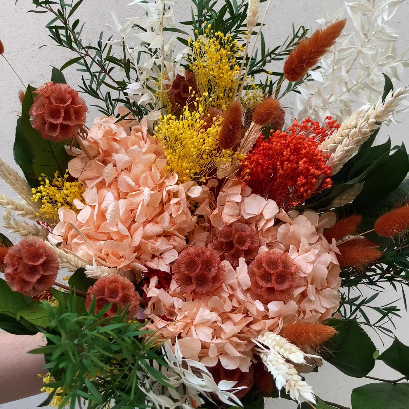 Bouquet en fleurs stabilisées éternelles orange et vert composé de Hortensia, scabieuse, blé, Lepto, Ruscus, Broom, Lagurus, Salal. En mouvement