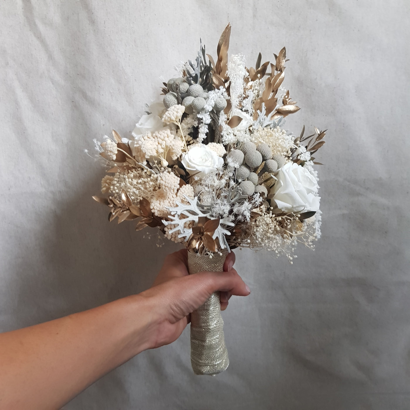 Bouquet de mariée en fleurs stabilisées éternelles blanc composé de Rose, Mini Gypsophile, Achilée, Cineraria, Ruscus, Brunia. Vu du côté gauche