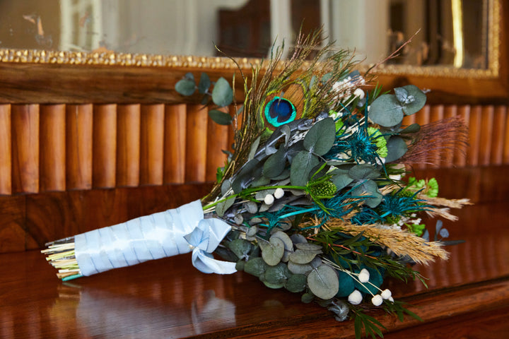 Bouquet de mariée en fleurs stabilisées éternelles bleu et blanc composé de Rose anglaise, Hortensia, Achilée, Pampa, Botao, Broom, Erygium, Lepto, Cinerea & Plume de Paon. Vu de côté