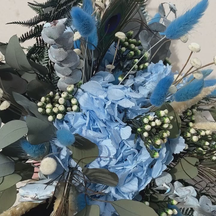 Bouquet de fleurs stabilisées éternelles bleu et vert composé d'Hortensia, Lagurus, Amarante, Ixodia, Botao, Fougère, Eucalyptus Populus, Eucalyptus Baby Blue & Plume de Paon. En mouvement 