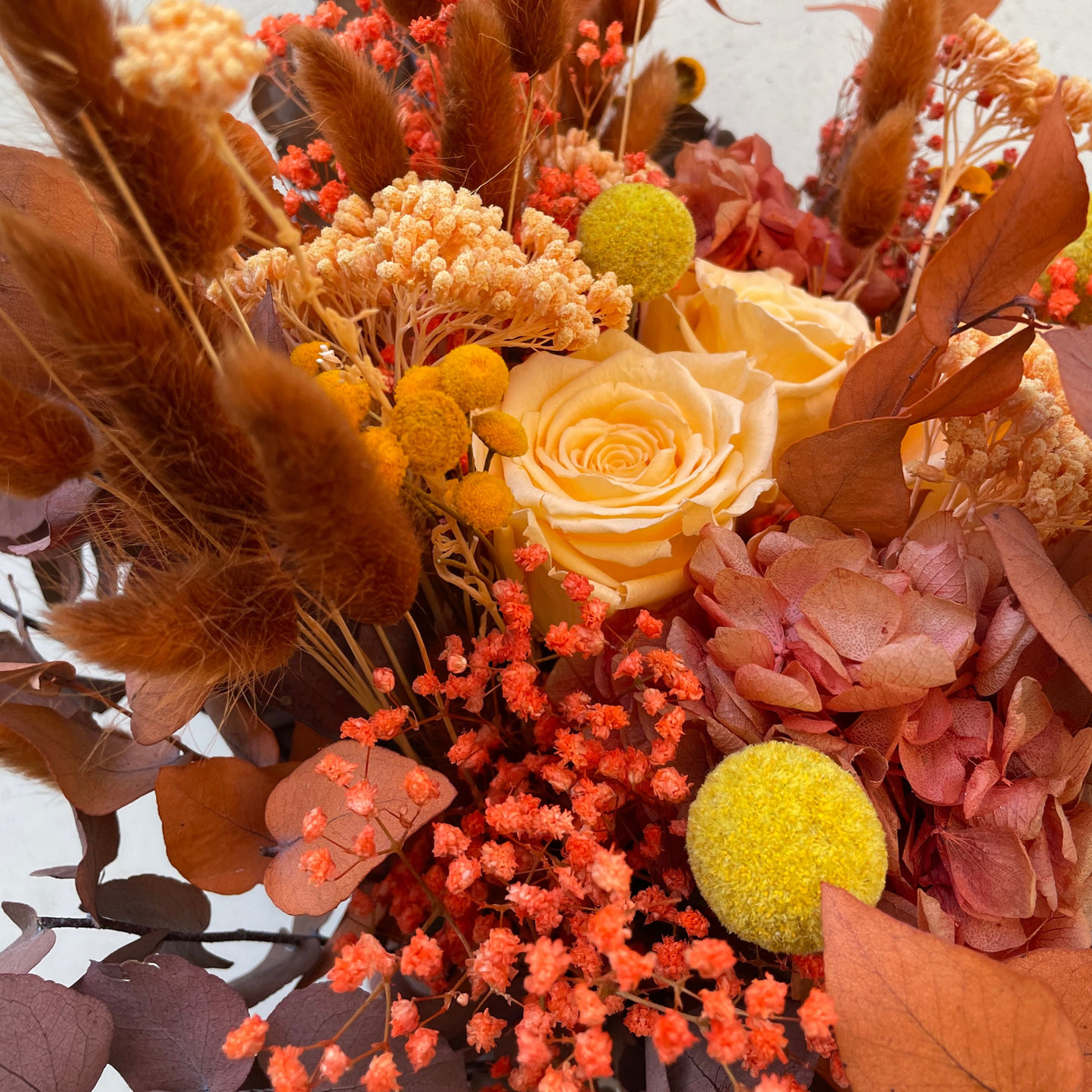 Bouquet de fleurs stabilisées éternelles orange composé de 3 Roses, Broom, Lagurus, Craspedia, Achillée, Botao, Eucalyptus Stuartiana. Vue du haut